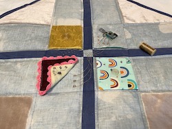 A quilt with 4 removable patches, one containing a microcontroller, and a spool of gold thread
